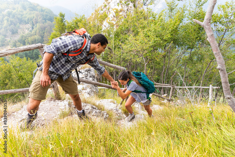 Italy, Massa, man helping a young woman to climb a step while hiking in the Alpi Apuane mountains
