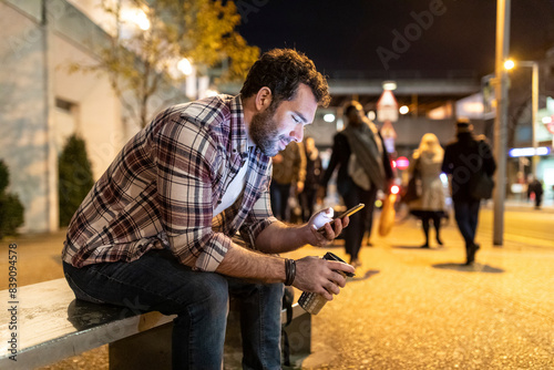 UK, London, smiling man sitting on a bench and looking at his phone by night photo