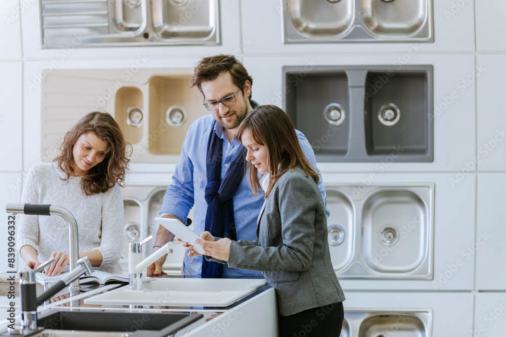 Customers consulting saleswoman in shop for kitchen sinks