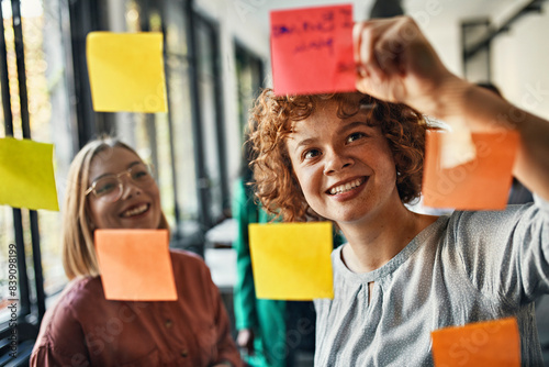 Happy colleagues with sticky notes at glass pane in office