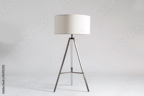 A modern table lamp with a tripod base in brushed metal and a white fabric shade on a solid white background, sleek and functional.