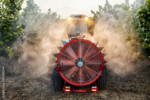 Canvas Print Rear view of agricultural vehicle with sprayer machine spraying hazel trees at countryside