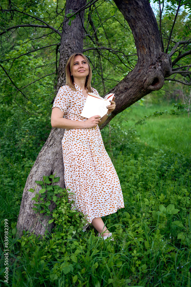 woman in a pastel dress reads a book near a tree in the garden, mockup woman in a pastel dress reads a book near a tree in the garden, mockup