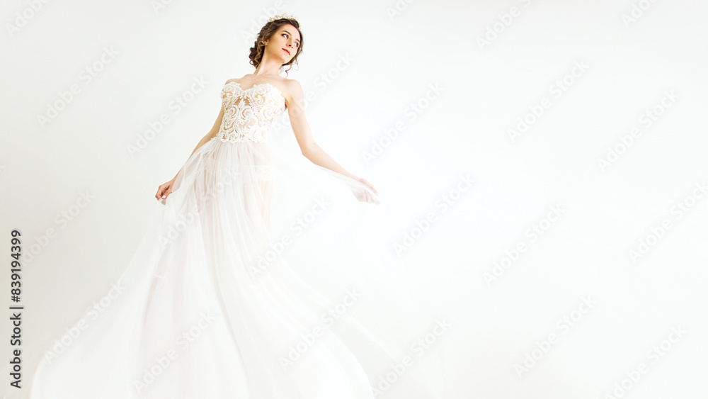 young smily brunette sexy girl in a white wedding boudoir dress and crown in hairstyle is dancing like swan princess in motion on a white wall background, free space on right side young smily brunette sexy girl in a white wedding boudoir dress and crown in hairstyle is dancing like swan princess in motion on a white wall background, free space on right side