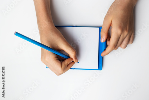 hand holding blue pencil and writing in notebook on white background isolated copy space photo