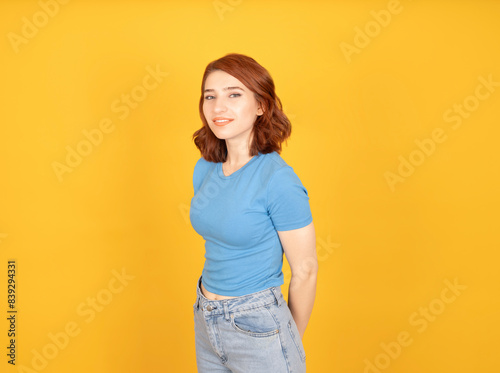 Confident cute woman, portrait of young caucasian red bob hair confident cute woman standing in casual outfit posing smiling pleased to camera. Yellow studio background, copy space.