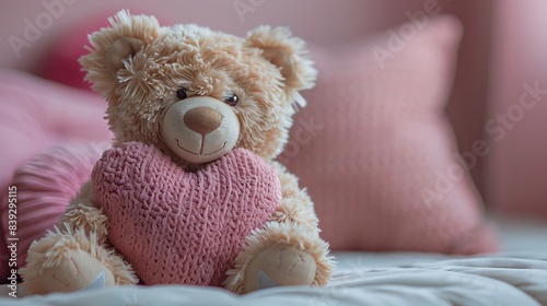 A teddy bear holding a heart-shaped pillow on a solid light pink background © Maher