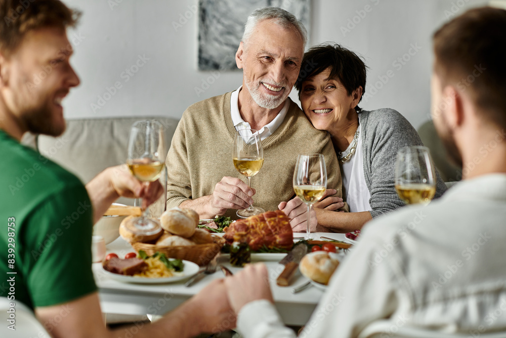A gay couple shares a celebratory dinner with their families, with smiles and wine glasses raised in a toast. A gay couple shares a celebratory dinner with their families, with smiles and wine glasses raised in a toast.