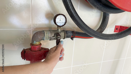 Red fire hydrant reel on a wall waiting for action. The hand holds onto the levers of the fire pump valve that hangs on the wall. photo