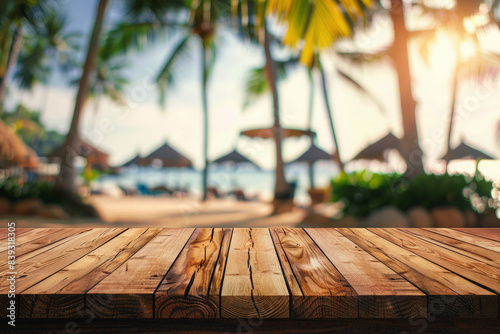 Wooden table top set against backdrop of tropical palm trees and sandy beach with thatched umbrellas in summer day