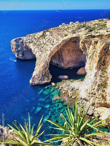 Heavenly resting place on the sea beach sand with large boulders. Legendary bridge lovers. Natural stone arch and sea caves and agave plant in foreground. Pleasure boat with tourists runs