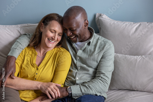 Senior carefree couple laughing together at home cuddling on the sofa photo