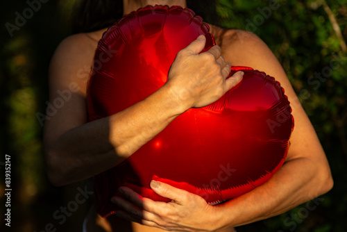 Mulher abraçando apaixonadamente um balão vermelho em forma de coração.