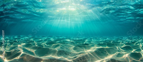 Underwater view of clear blue water with ripples and sand at the bottom, sunlight filtering through the surface.