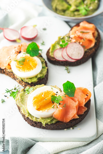 Salmon avocado toast with fresh radishes, avocado mousse, boiled egg, sesame seeds and fresh herbs, nasturtiums and black rye bread. Summer, healthy breakfast, lunch, easy recipes, front view