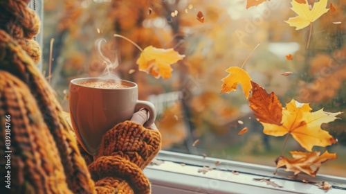 Fototapeta Naklejka Na Ścianę i Meble -  Imagine a cozy autumn scene with a person sitting by the window, holding a mug of pumpkin spice latte, watching leaves fall gently outside.
