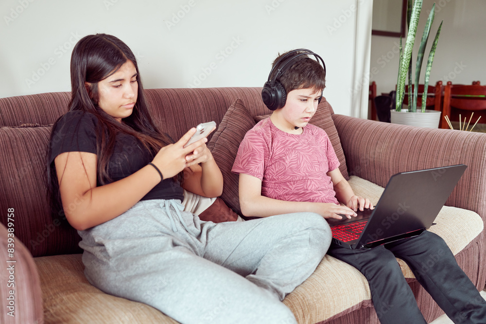 teen girl and preteen boy sitting on the sofa of the living room using technology teen girl and preteen boy sitting on the sofa of the living room using technology