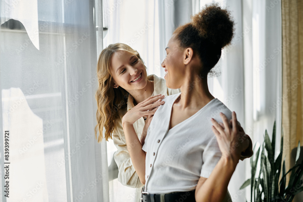 Fototapeta premium Two women, a diverse lesbian couple, smile at each other while spending time together at home.