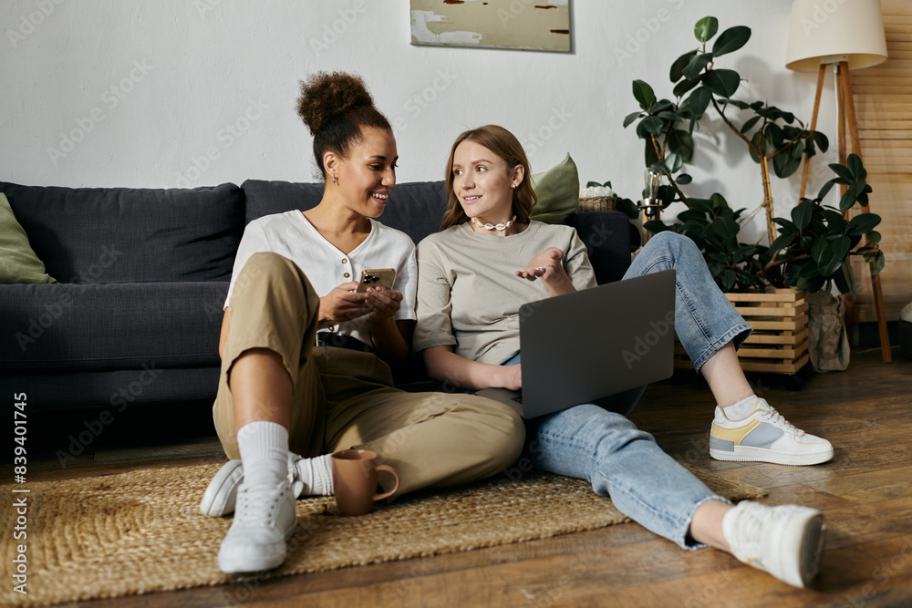 A lesbian couple relaxes at home, one using a laptop, the other on their phone. A lesbian couple relaxes at home, one using a laptop, the other on their phone.