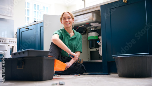 Portrait Of Female Plumber With Digital Tablet Fixing Waste Disposal Unit In Domestic Kitchen Sink photo