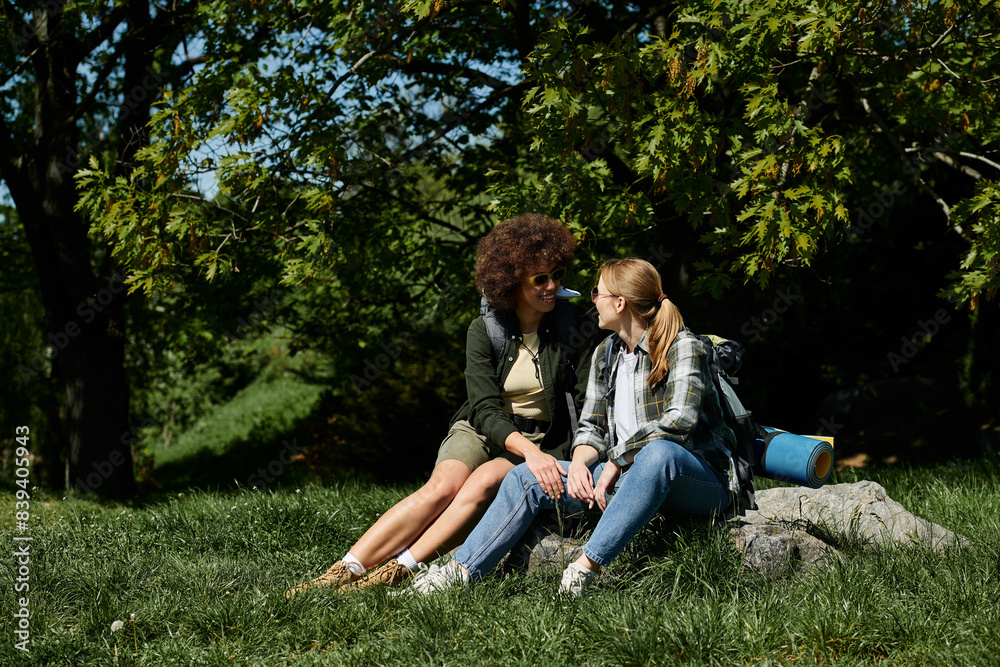 A young, multicultural lesbian couple sits together on a rock in the woods, enjoying a break from their hike. A young, multicultural lesbian couple sits together on a rock in the woods, enjoying a break from their hike.