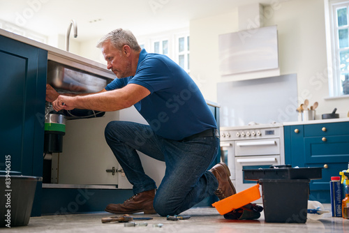 Mature Male Plumber Fixing Waste Disposal Unit In Domestic Kitchen Sink photo