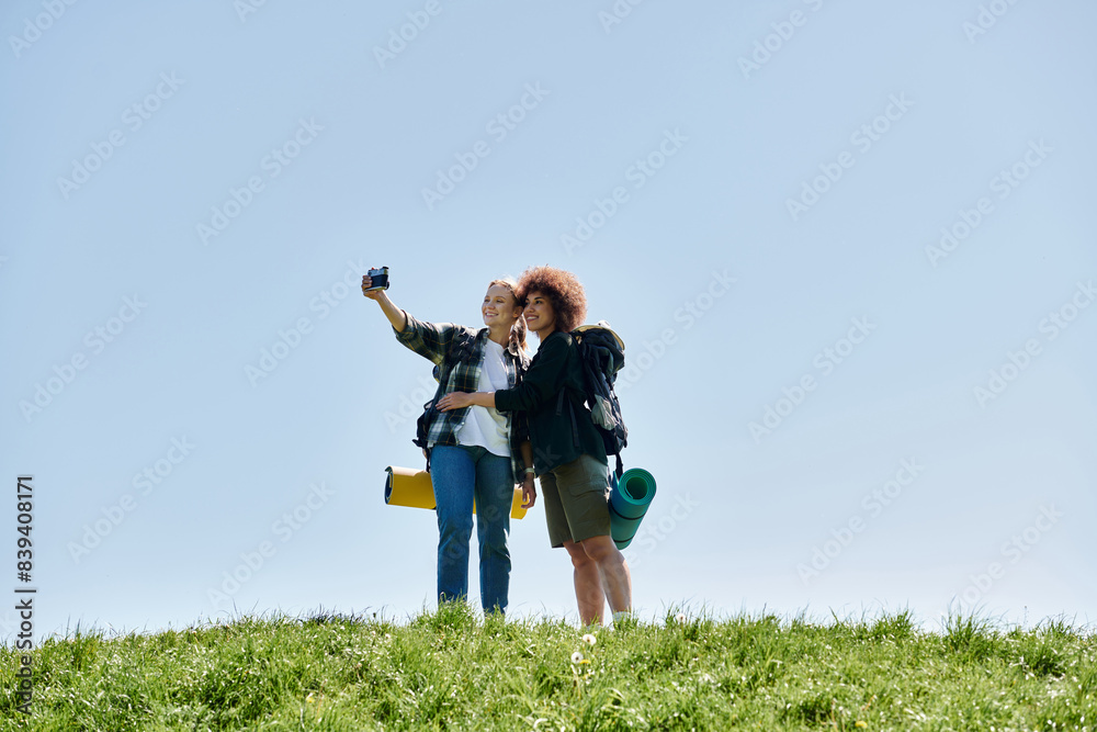 Two young women, a lesbian couple, hike together in the wilderness and take a selfie on a grassy hill. Two young women, a lesbian couple, hike together in the wilderness and take a selfie on a grassy hill.