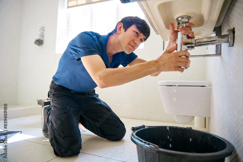 Male Plumber Fixing Leak In Domestic Bathroom Sink Or Basin Male Plumber Fixing Leak In Domestic Bathroom Sink Or Basin