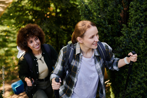 A young lesbian couple smiles while hiking through a lush green forest together. © Bliss