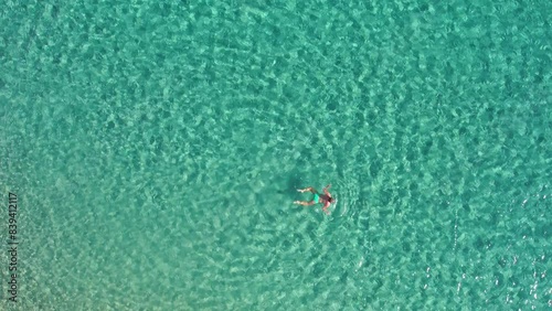 Woman swimming in emerald green waters of Sardinia Mediterranean sea. Summer relax and leisure. Top down aerial drone shot