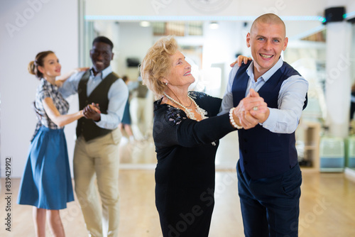 Man and elderly woman performing ballroom dance in dancing room