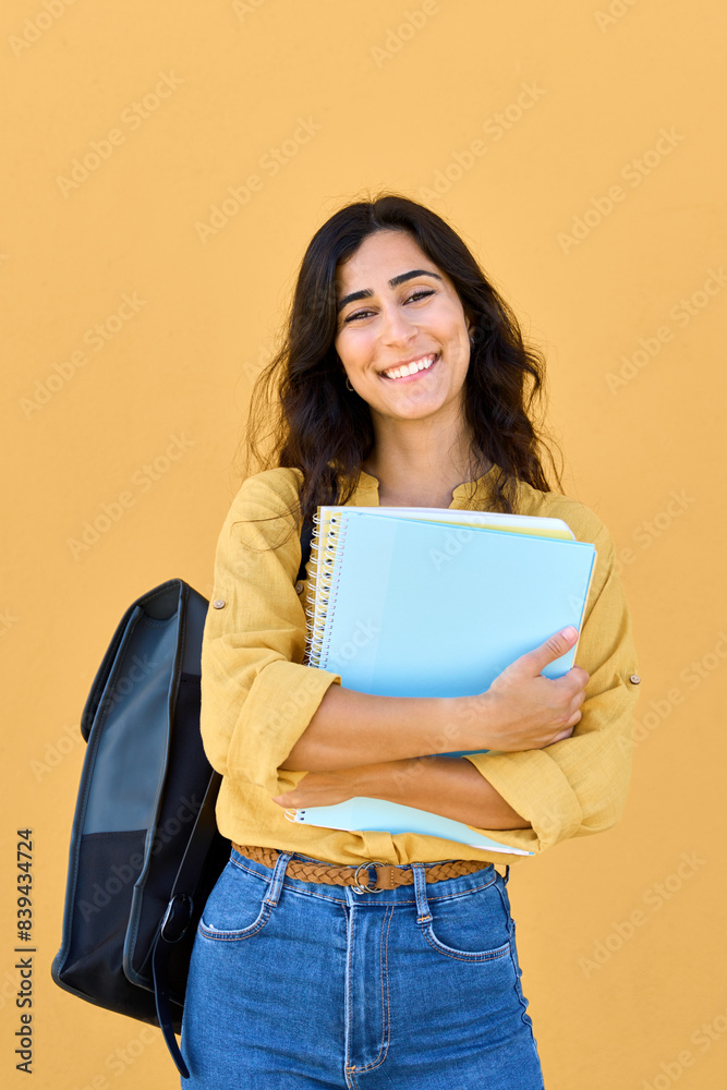 Young Arabian or Indian holding books, notebooks for studying. Smiling vertical portrait of beautiful middle eastern Israel girl student with backpack isolated on yellow background looking at camera. Young Arabian or Indian holding books, notebooks for studying. Smiling vertical portrait of beautiful middle eastern Israel girl student with backpack isolated on yellow background looking at camera.