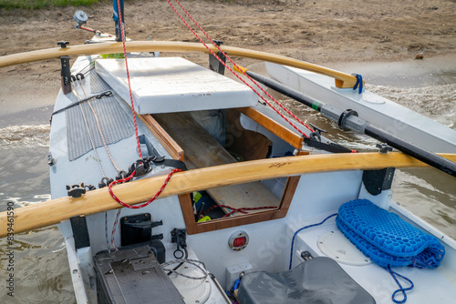 detail of a homebuilt sailing and rowing trimaran boat with a small cabin and sliding rowing seat