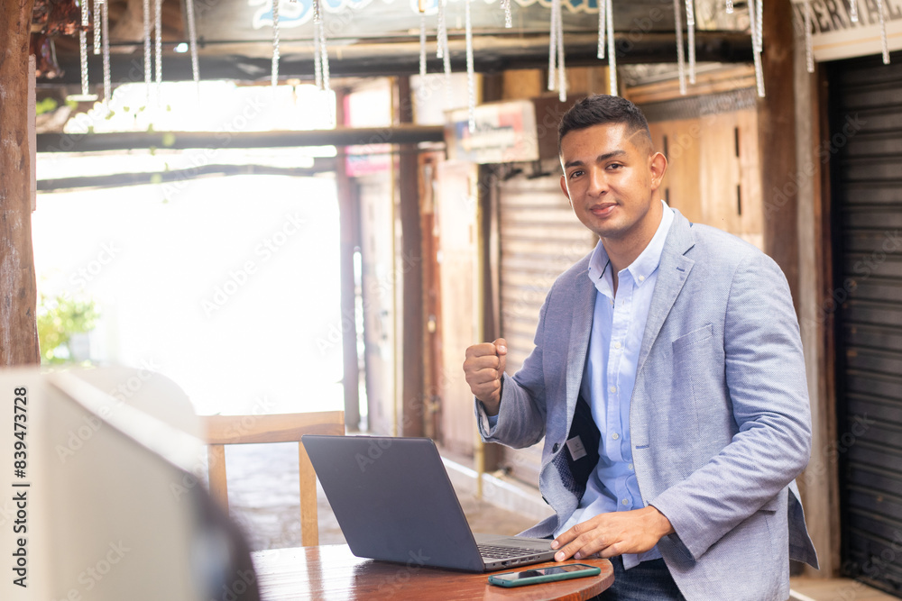 Fototapeta premium young latin freelance man with cell phone and laptop working in a beautiful town with elegant suit