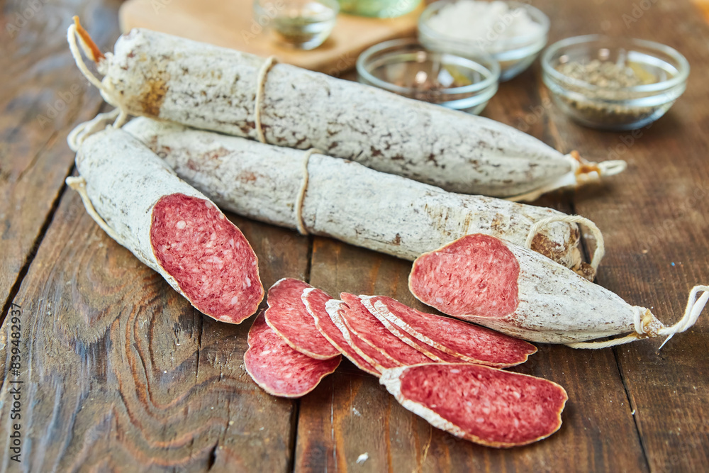 The cured sausage, cut into slices, lies on a wooden surface surrounded by spices. Meat production. The cured sausage, cut into slices, lies on a wooden surface surrounded by spices. Meat production.
