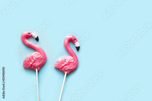 Two pink flamingo candy lollipops on blue background. Food and snacks for kids Top view. Space for text.