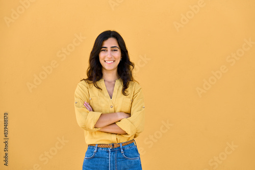 Portrait of middle eastern Israel girl student standing with crossed arms isolated on yellow background. Smiling young Arabian Indian woman, businesswoman, business lady looking at camera, copy space