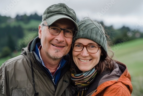 Portrait of a blissful caucasian couple in their 30s wearing a functional windbreaker while standing against quiet countryside landscape
