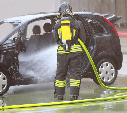 Firefighter extinguishing car fire with foam jet and oxygen cylinder photo