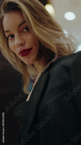 Portrait of a confident woman wearing bold red lipstick and a stylish black blazer, looking directly at the camera in an indoor setting. Confident Woman with Red Lipstick in Stylish Black. Vertical.