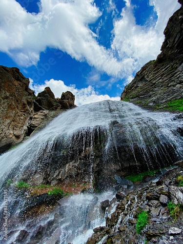 Waterfall in the mountains with green hrebats and blue sky white clouds