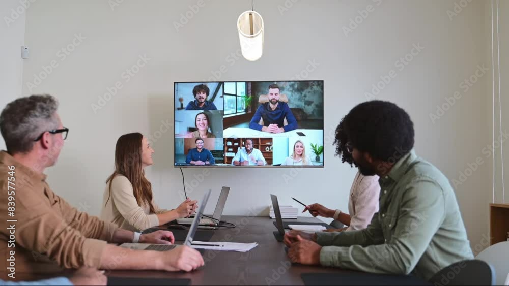 A team of professionals engaged in a productive video conference, combining in-person and remote participants on a large screen in a conference room. Effective communication tools in achieving goals