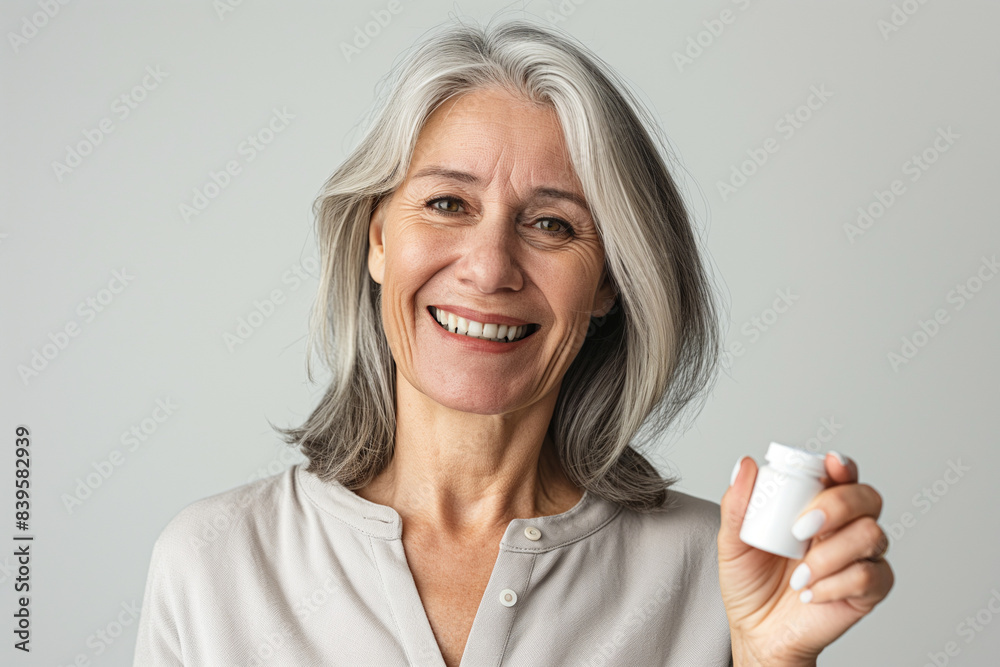 a Smiling adult woman of 65 years old stands on a white background, the woman is holding a white bottle of capsules in her right hand, the camera is close up focused on the bottle and her face, a Smiling adult woman of 65 years old stands on a white background, the woman is holding a white bottle of capsules in her right hand, the camera is close up focused on the bottle and her face,