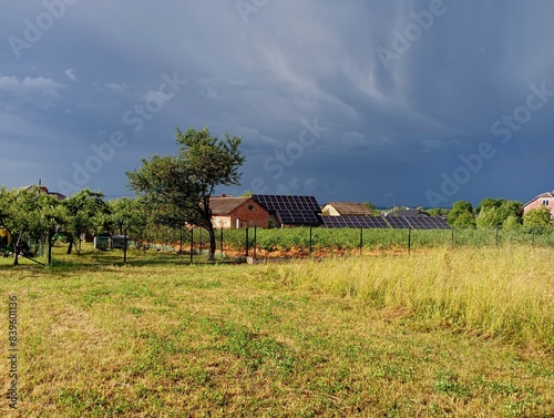 A cargo cloud is visible above the village. a beautiful landscape of fields with yellow grass and a house equipped with solar panels during a thunderstorm. The topic of changes in temperature phenomen photo