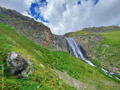 Waterfall in the mountains with green hrebats and blue sky white clouds, Elbrus region
