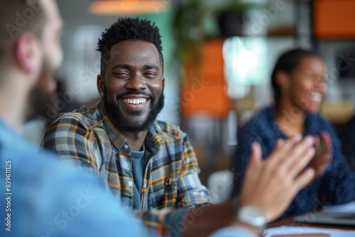 Man in plaid shirt smiles at table with fellow people © Sandu