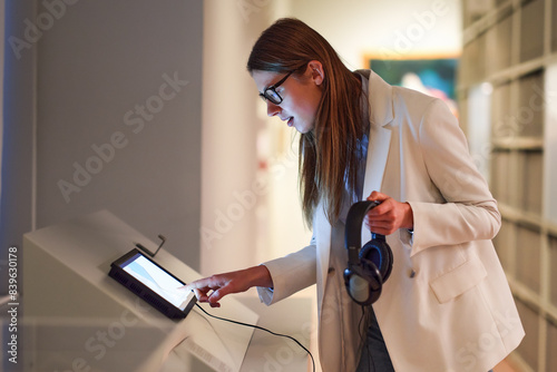 Woman wearing headphones and contemplates ancient arts. Student visiting gallery or museum. Concept of modern education and culture.