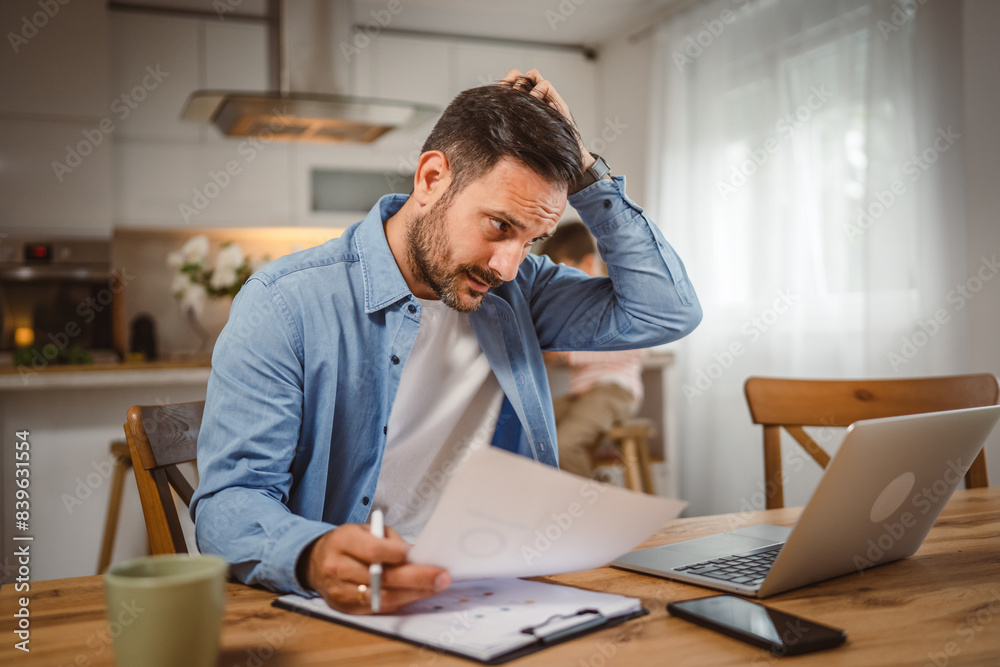 Exhausted man father work at home on laptop with son in the background Exhausted man father work at home on laptop with son in the background