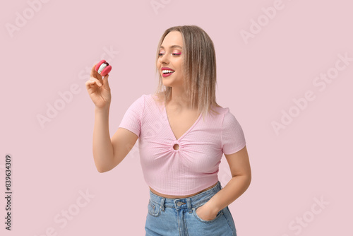 Happy young woman with sweet macaroon on pink background