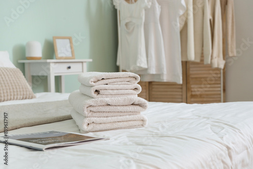 Stack of white clean towels and magazine on bed in bedroom